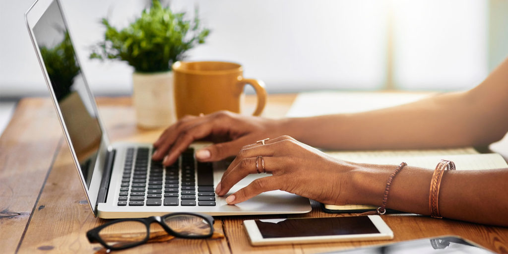 Person typing on silver laptop with caramel colored coffee cup on the desk.