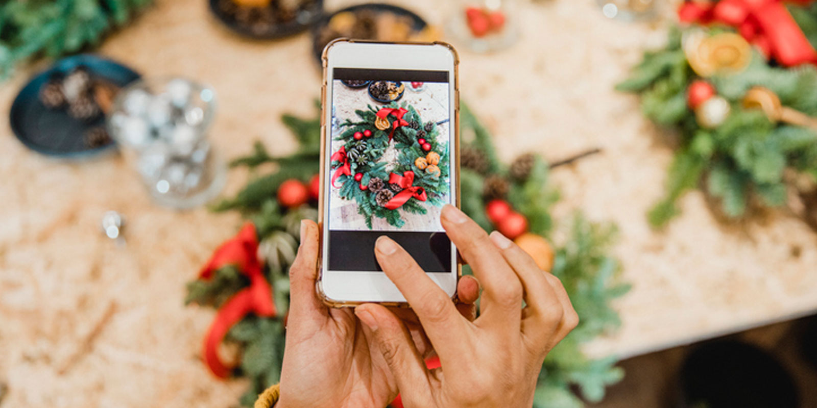 Person holding a phone taking a picture of a Christmas wreath.