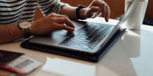 Person typing on a silver laptop with a white coffee mug next to them.