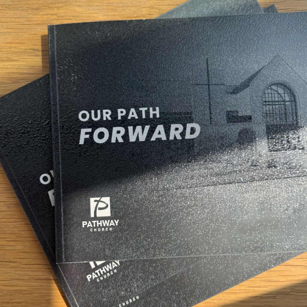 A stack of booklets titled "Our Path Forward" from Pathway Church, featuring a black textured cover with a faint building image and the church’s logo—a standout example of print design crafted for a Goff Companies case study.