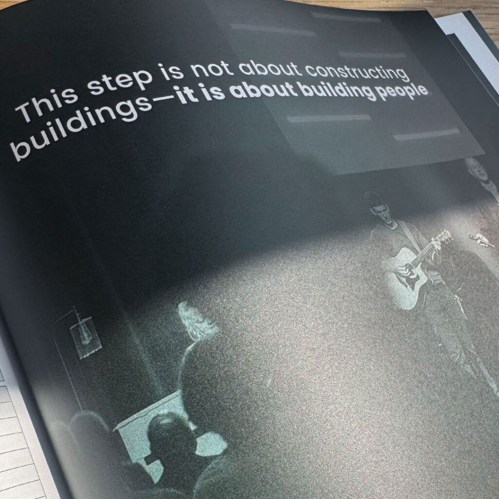 A booklet page by Goff Companies with the text, "This step is not about constructing buildings—it is about building people," above a black-and-white photo of people, including a person playing guitar, showcases thoughtful print design.