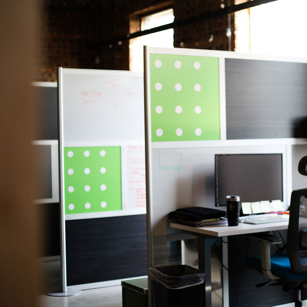 A modern office cubicle with a computer, office chair, desk items, and green panels with white polka dots on partition walls reflects an ardent focus on brand evolution and creative logo design.
