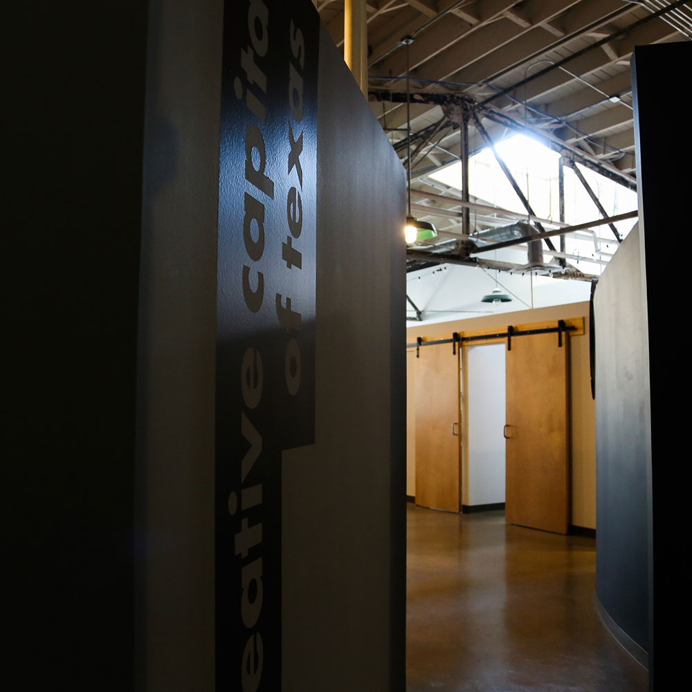 A view of an industrial-style hallway with high ceilings, wooden doors, and a partially visible sign reading "creative capitol of texas," reflecting the bold branding and vision of Designing Ardent.