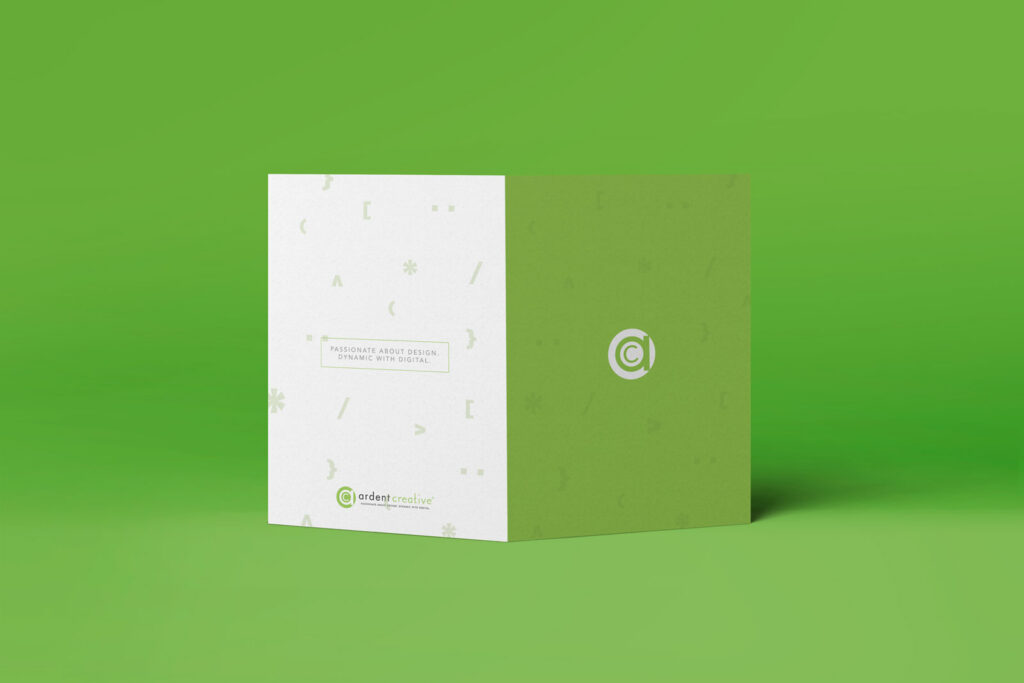 A folded brochure stands on a green surface; one side is white with faint icons and text, the other is solid green featuring Ardent’s circular logo at its center—showcasing thoughtful designing and branding.