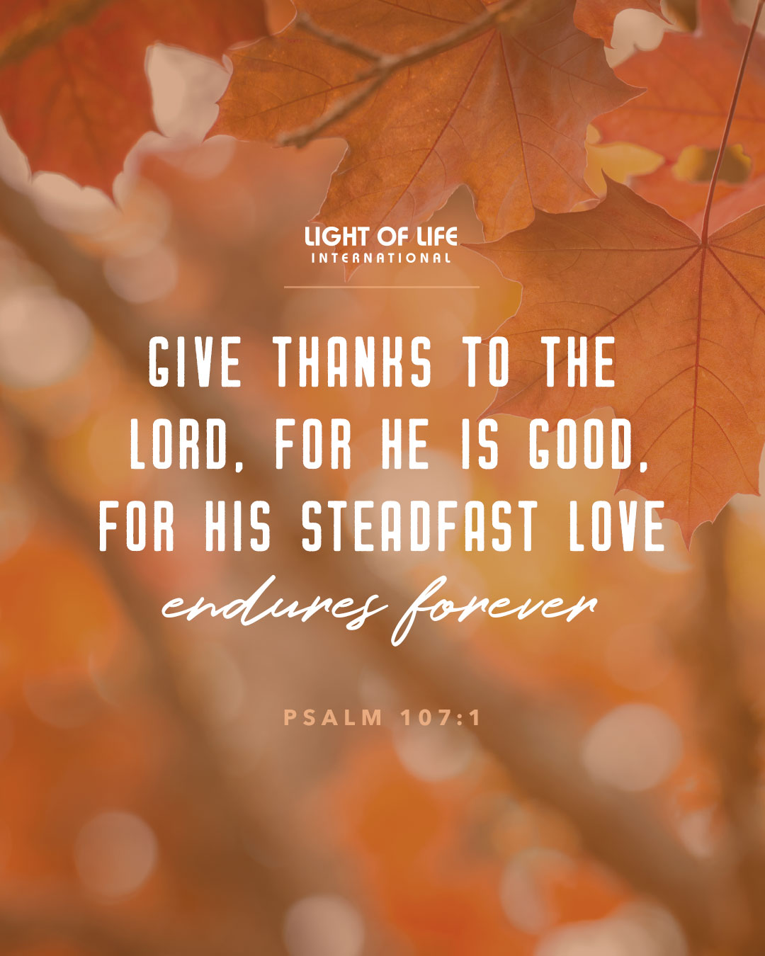 Close-up of autumn leaves with the Bible verse Psalm 107:1 overlaid, perfect for faith-based branding and encouraging thanks to the Lord for his steadfast love.
